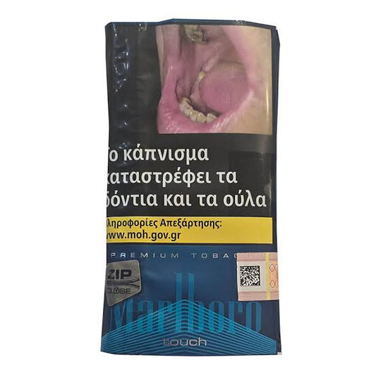 A pack of Marlboro Touch premium tobacco in Greek, featuring a dark blue and black design with a health warning graphic of an open mouth and a yellow banner with the website www.moh.